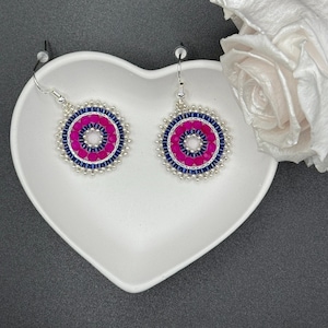 Könnte beinhalten: Ein Paar silberne Ohrhänger mit rosafarbenen und blauen Perlenkreisen. Die Ohrringe haben einen silbernen Hakenverschluss.