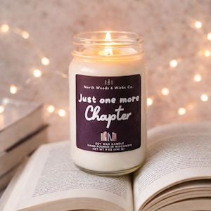 K&ouml;nnte beinhalten: Eine brennende Sojawachskerze in einem Glas mit einem lila Etikett mit der Aufschrift "Just one more Chapter". Die Kerze steht auf einem offenen Buch. Die Kerze ist handgegossen in Wisconsin und wiegt 198 g.