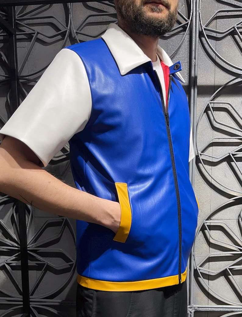 May include: A short-sleeved jacket made of blue faux leather with a white collar and sleeves. The jacket features a black front zipper, yellow trim along the bottom hem, and yellow accents on the two side pockets. A red inner lining is visible.