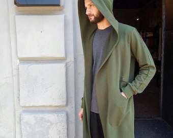 May include: A long, green hooded cardigan with a relaxed fit. The cardigan has a deep hood and a long, flowing hem. The model is wearing the cardigan over a grey t-shirt and black trousers.