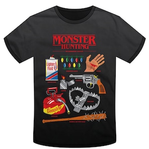 Puede incluir: Camiseta negra con el texto rojo "MONSTER HUNTING" e ilustraciones de suministros para la caza de monstruos. Incluye un encendedor, una lata de gasolina, luces de Navidad, un revólver, una trampa para osos y un bate de béisbol con clavos.