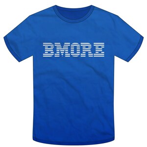 May include: Royal blue t-shirt with the word "BMORE" in white, stylized, horizontal lines. The shirt has a crew neck and short sleeves. The text is centered on the front of the shirt.
