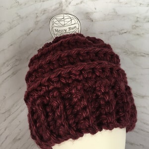May include: A burgundy crocheted beanie with a white tag that says "Messy Bun".