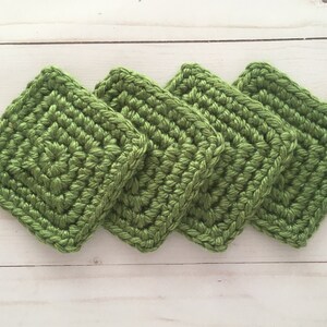 May include: Four green crocheted squares, stacked on top of each other.