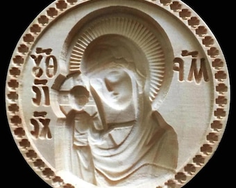 May include: A carved wooden religious icon depicting a woman and child, surrounded by a decorative border. The icon features detailed relief carving and text in an unknown language. The overall design is circular, with a natural wood color.