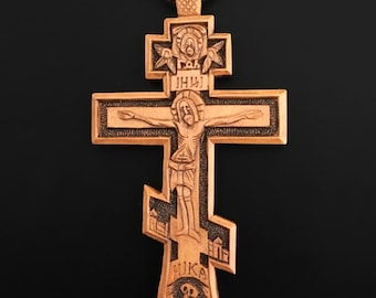 May include: A wooden Orthodox cross pendant with intricate carvings. The cross features a depiction of Jesus Christ on the front, with the inscription "IHС" above him. The back of the cross features a skull and crossbones, with the inscription "NIKA" below.