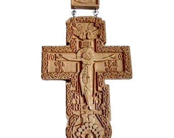 May include: A carved wooden Orthodox cross with detailed carvings. The cross depicts Jesus Christ at the centre, with religious symbols and inscriptions. It hangs from a wooden top piece with a carved image, suspended by a cord.