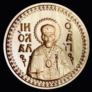 May include: A circular wooden carving of a religious figure, possibly a saint, with a halo and detailed features. The carving includes text in an older script around the figure. The border is decorated with a repeating cross pattern.