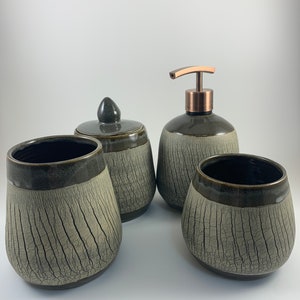 Puede incluir: Conjunto de cuatro accesorios de baño de cerámica en un esmalte craquelado gris y negro. El conjunto incluye un dispensador de jabón, un tarro con tapa y dos vasos.