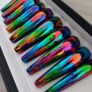 May include: A set of long, iridescent press-on nails. Each nail is a vibrant mix of colors, including blue, green, orange, and purple, creating a unique, oil-slick effect. The nails are displayed in a white box, showcasing their glossy finish.