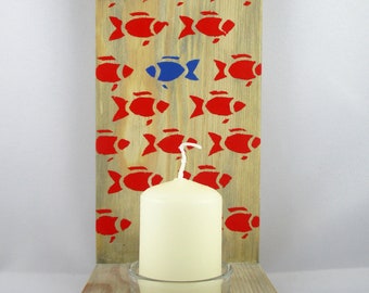 May include: A wooden candle holder with a single candle in a glass holder. The holder is decorated with a pattern of red fish, with one blue fish in the center.