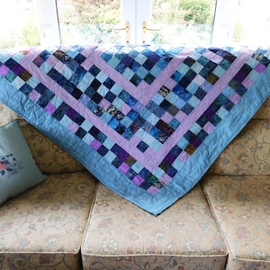 May include: A blue and purple patchwork quilt with a light blue border, folded on a floral patterned sofa.