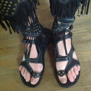 Puede incluir: Sandalias gladiadoras de cuero negro con flecos y tachuelas met&aacute;licas. Las sandalias tienen una correa sobre el pie y un bucle para el dedo del pie.
