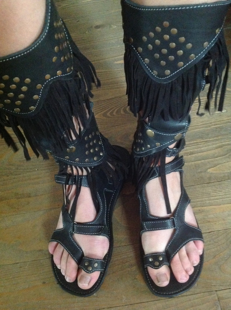 Puede incluir: Sandalias gladiadoras de cuero negro con flecos y tachuelas met&aacute;licas. Las sandalias tienen una correa sobre el pie y un bucle para el dedo del pie.