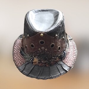 May include: A black leather fedora hat with a brown leather band, metal accents, and feathers. The hat has a distressed look and is decorated with eyelets.