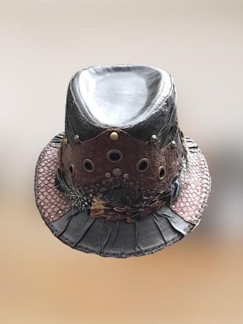 May include: A black leather fedora hat with a brown leather band, metal accents, and feathers. The hat has a distressed look and is decorated with eyelets.