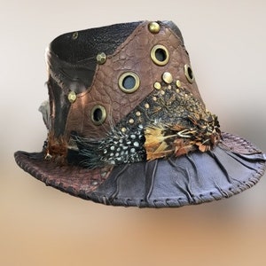 May include: A brown leather hat with a wide brim, decorated with feathers and metal accents. The hat is made of different pieces of leather sewn together.
