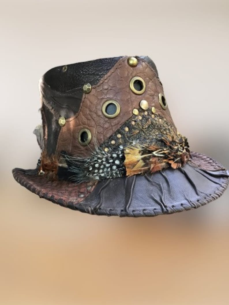 May include: A brown leather hat with a wide brim, decorated with feathers and metal accents. The hat is made of different pieces of leather sewn together.