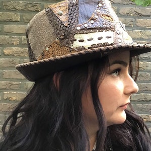 May include: A brown leather hat with a patchwork design. The hat is made of different types of leather, including suede, snakeskin, and embossed leather. The hat has a wide brim and a tall crown.