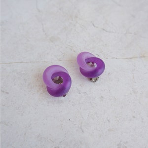 May include: A pair of purple, frosted, resin earrings in the shape of a twisted circle.