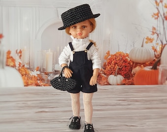 May include: A doll wearing a black hat, dungarees, and shoes, carrying a black handbag. The doll is dressed in a white long-sleeved shirt and patterned tights. The background features pumpkins, autumn leaves, and a decorative fireplace.