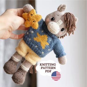 May include: A handmade knitted horse doll with a star-shaped toy. The horse has a blue sweater with a yellow star, tan shorts, and brown boots. The doll is holding a yellow star. The image includes the text "KNITTING PATTERN PDF" and a US flag.