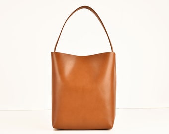 Puede incluir: Un bolso tote de cuero marrón con un solo asa superior.
