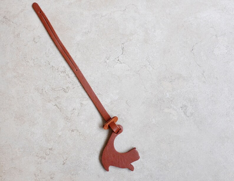 Peut inclure: Un marque-page en cuir marron avec un motif d&eacute;coup&eacute; en forme d'oiseau. Le marque-page est attach&eacute; avec une ficelle en cuir marron.