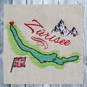 Puede incluir: Diseño bordado del lago de Zúrich, Suiza. El lago está delineado en verde y azul, con un corazón rojo marcando una ubicación en el lago. La bandera suiza está en la esquina inferior izquierda, y la palabra "Zurichsee" está bordada en cursiva roja.