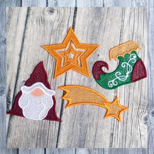 May include: Embroidered Christmas-themed patches in various shapes. Includes a star, a shooting star, a gnome, and an elf shoe. The patches are in shades of orange, green, red, and white, with intricate stitching details. The patches are on a wooden background.