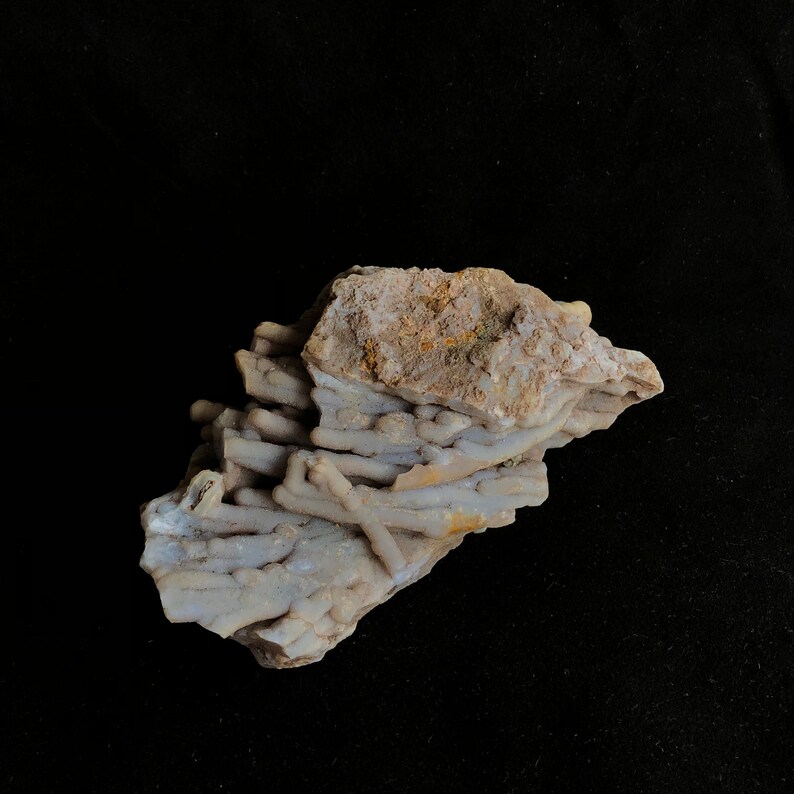 K&ouml;nnte beinhalten: Nahaufnahme einer hellbraunen und wei&szlig;en Achat-Geode mit einem Cluster aus wei&szlig;en, nadelf&ouml;rmigen Kristallen. Die Geode hat eine raue, strukturierte Oberfl&auml;che.