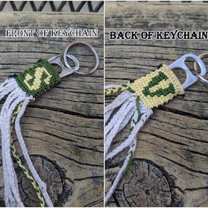 May include: A green and yellow woven keychain with a metal ring and a pull tab from a beverage can. The keychain has a fringe on the bottom. The text "FRONT OF KEYCHAIN" and "BACK OF KEYCHAIN" are visible in the image.