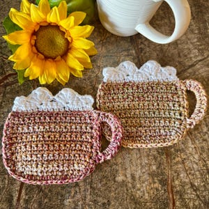 May include: Two crocheted mug rugs in the shape of a coffee mug. One is brown and beige with a white crocheted rim. The other is red, brown, and beige with a white crocheted rim.