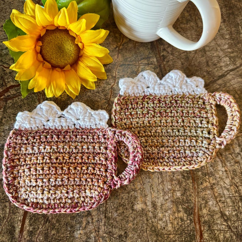 May include: Two crocheted mug rugs in the shape of a coffee mug. One is brown and beige with a white crocheted rim. The other is red, brown, and beige with a white crocheted rim.