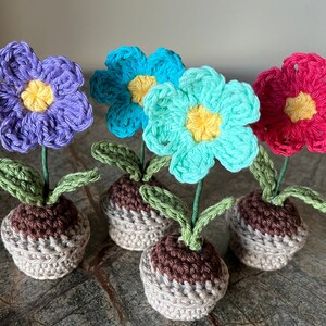 May include: Four crocheted flower pots with different colored flowers. The flowers are purple, blue, turquoise, and pink. The pots are brown and beige.