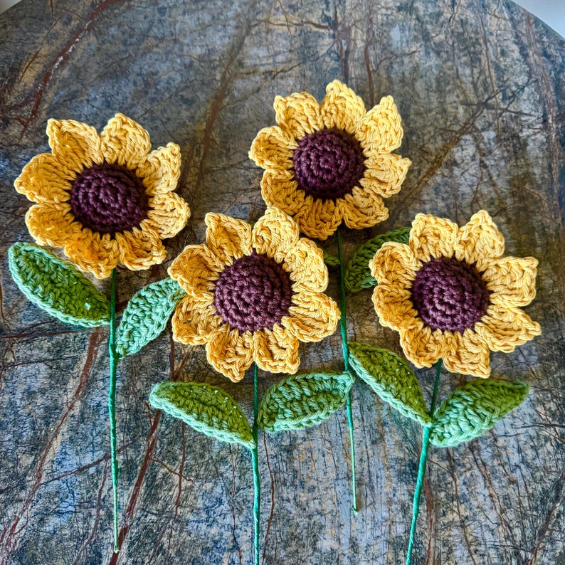 May include: Four crocheted sunflowers with brown centers and green stems and leaves.