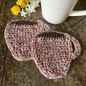 May include: Two crocheted cup coasters in a red and white pattern. The coasters are shaped like a coffee cup with a handle.