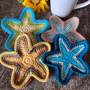 May include: A collection of handmade crochet starfish coasters in various colors. The coasters feature shades of blue, yellow, tan, and green. Each coaster has a unique color pattern and design, perfect for adding a touch of coastal charm to any home.