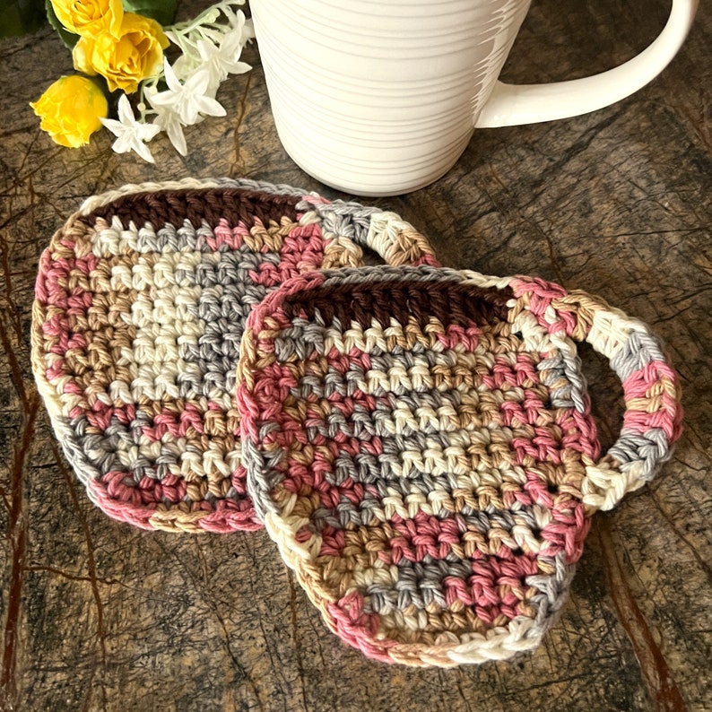 May include: Two crocheted coasters in pink, brown, beige, and gray. One coaster has a handle.