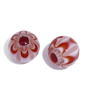 May include: Two round beads with a floral design. The beads are a light pink colour with a swirling pattern of red and white. Each bead has a dark red centre and a hole for stringing.