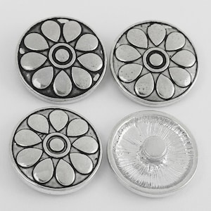 May include: Four circular silver-toned buttons featuring a raised floral pattern with eight petals surrounding a central circle. Three buttons display the decorative front, while one button shows the plain, textured reverse side with a central shank.