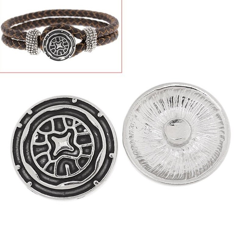 May include: A brown braided leather bracelet with a silver-toned circular clasp featuring a black recessed geometric pattern and two beaded silver-toned accents. Also shown are two views of the circular silver-toned button with a black center.