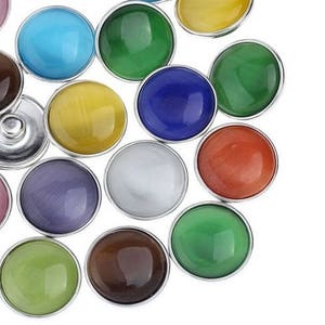 May include: Assortment of colorful round snap buttons with silver metal settings. The buttons are in various colors, including pink, blue, green, yellow, brown, red, and white.