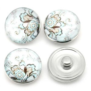 May include: Four round snap buttons featuring a light blue, white, and brown floral paisley pattern under a smooth glass dome. Three buttons display the patterned top, while one button is flipped to show the silver metal snap fastener mechanism.