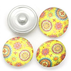 May include: Three circular snap buttons with a bright yellow background featuring a repeating pattern of colorful, intricate geometric star and circular motifs in shades of red, orange, blue, and green, alongside one plain silver metal snap button.