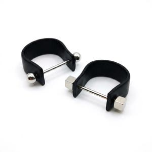May include: Two black U-shaped cuffs featuring a metallic bar across the opening. One cuff is secured with two polished silver-tone spherical ends, while the other cuff is secured with two polished silver-tone cube-shaped ends on the metal bar.