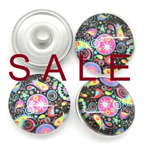 May include: Four round snap buttons with a colorful paisley design on a black background. The design includes pink, blue, yellow, and green elements. The word "SALE" is superimposed in red. One button is silver, and the others have a silver rim.