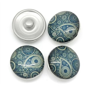 Könnte beinhalten: Vier runde Druckknöpfe mit einem blau-türkisfarbenen Paisley-Muster, das komplexe florale und kreisförmige Motive aufweist. Ein Knopf zeigt die silberne Metallunterseite mit einem Mittelstift, während drei die gemusterte Oberseite zeigen.