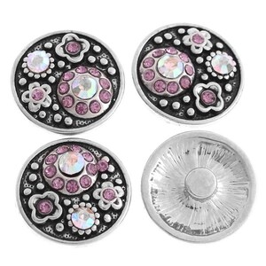 Könnte beinhalten: Vier silberfarbene Druckknöpfe mit rosa Strasssteinen und Blumendesigns. Die Knöpfe sind rund und haben ein erhabenes Design.