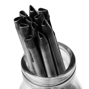 Könnte beinhalten: Nahaufnahme eines Glasbehälters, gefüllt mit einem Bündel schwarzer Metall-Stanzwerkzeuge mit spitzen Spitzen.